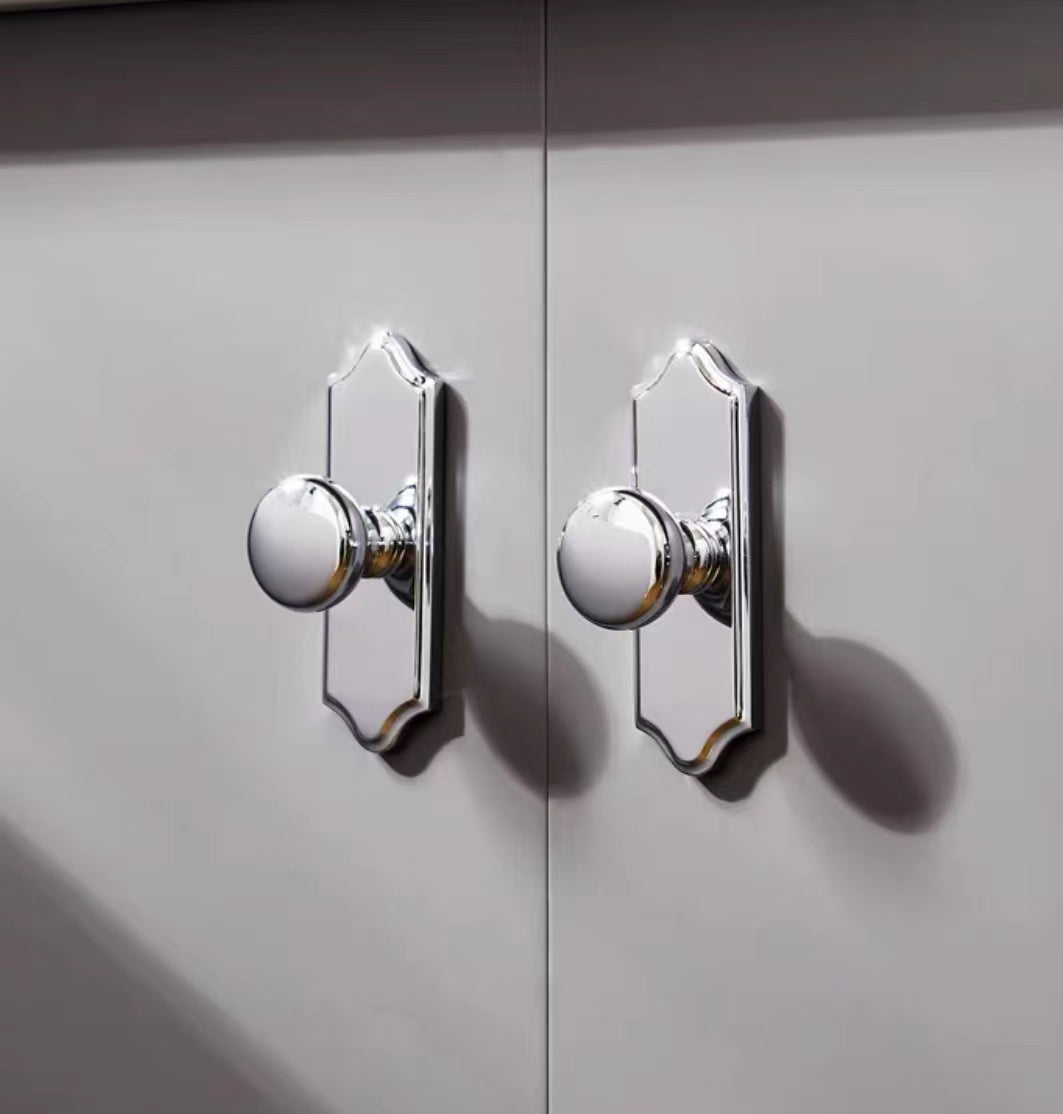 Close-up of two round shiny silver door knobs on a gray cabinet.