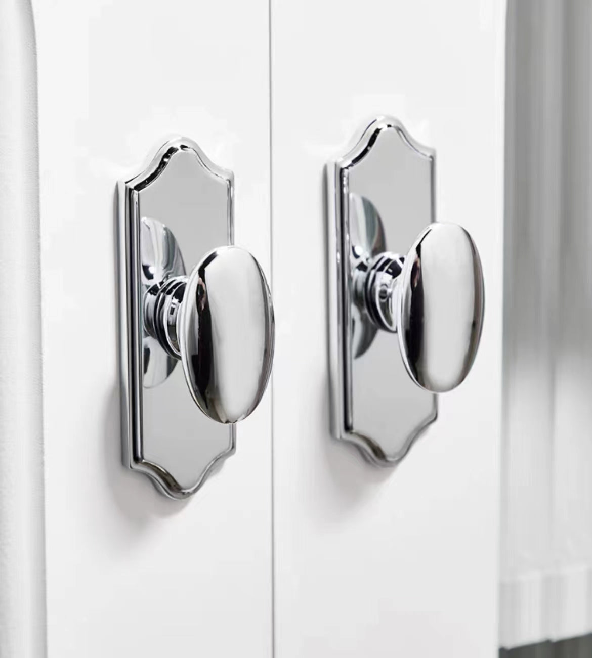Close-up of two polished chrome oval door pulls on a white door.