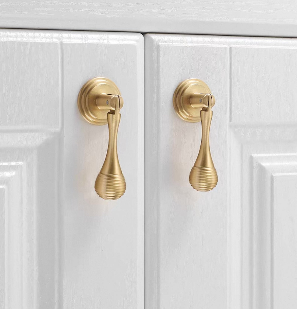 Close-up of two gold cabinet drop pulls on a white cabinet door.