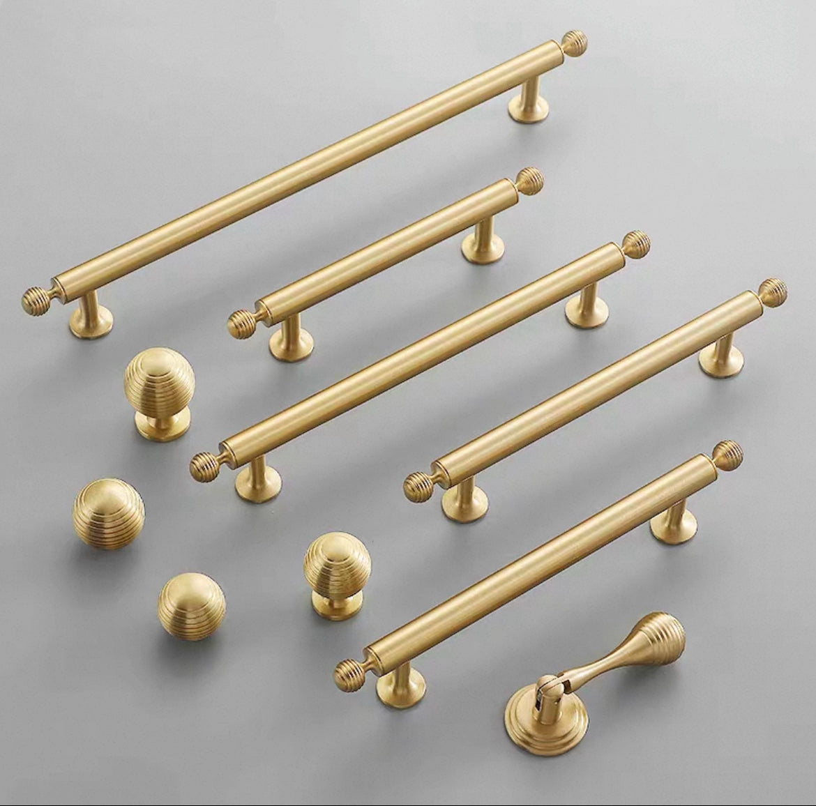Set of brushed gold brass cabinet handles and round knobs on a gray background