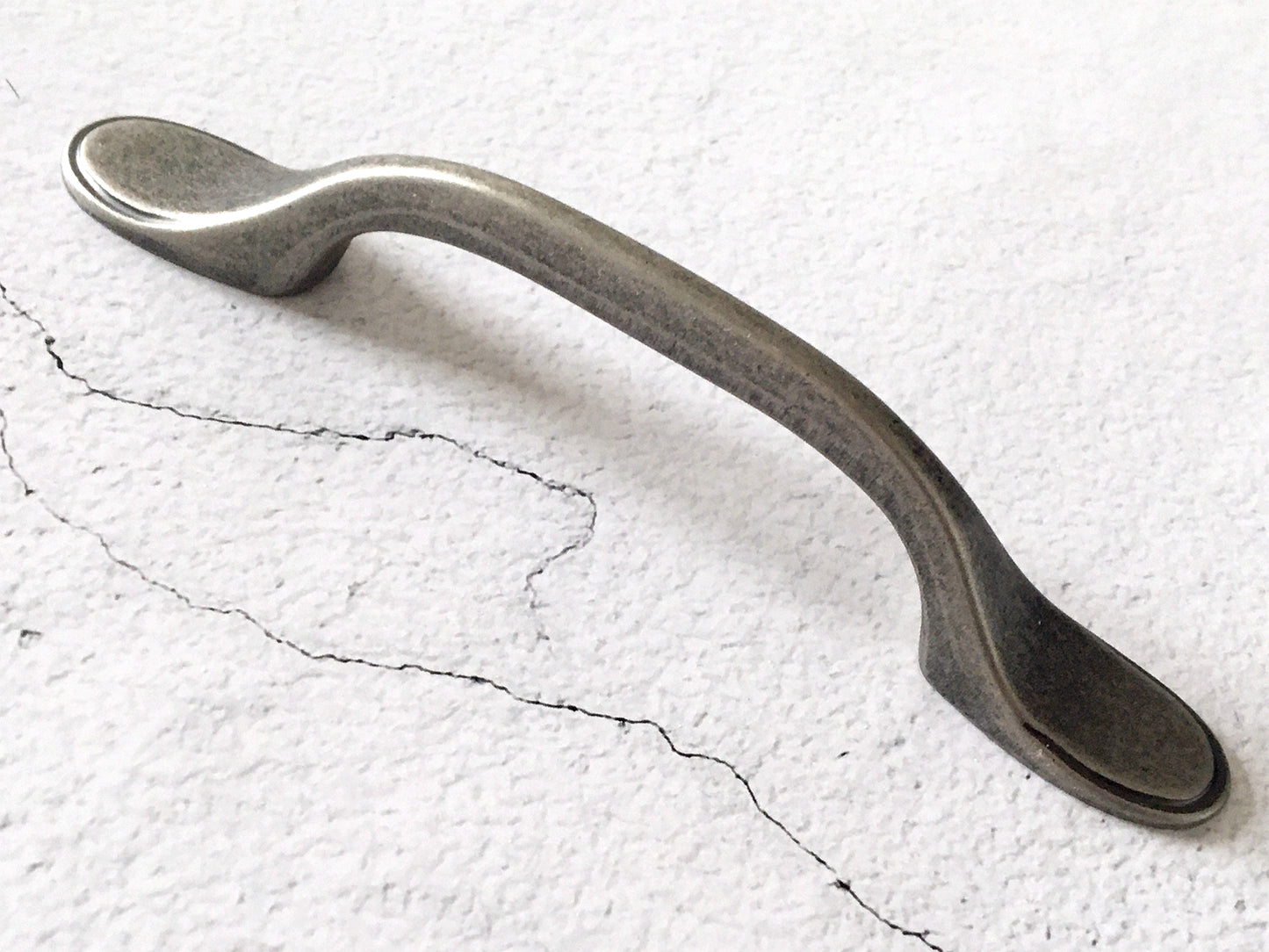 Pewter cabinet handle on a textured white surface