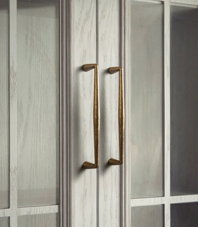 Close-up of rustic antique brass handles on a cabinet door.