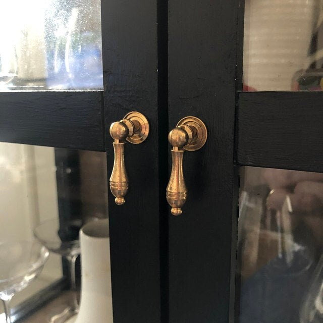 Black cabinet with gold teardrop pendant handles in a kitchen setting