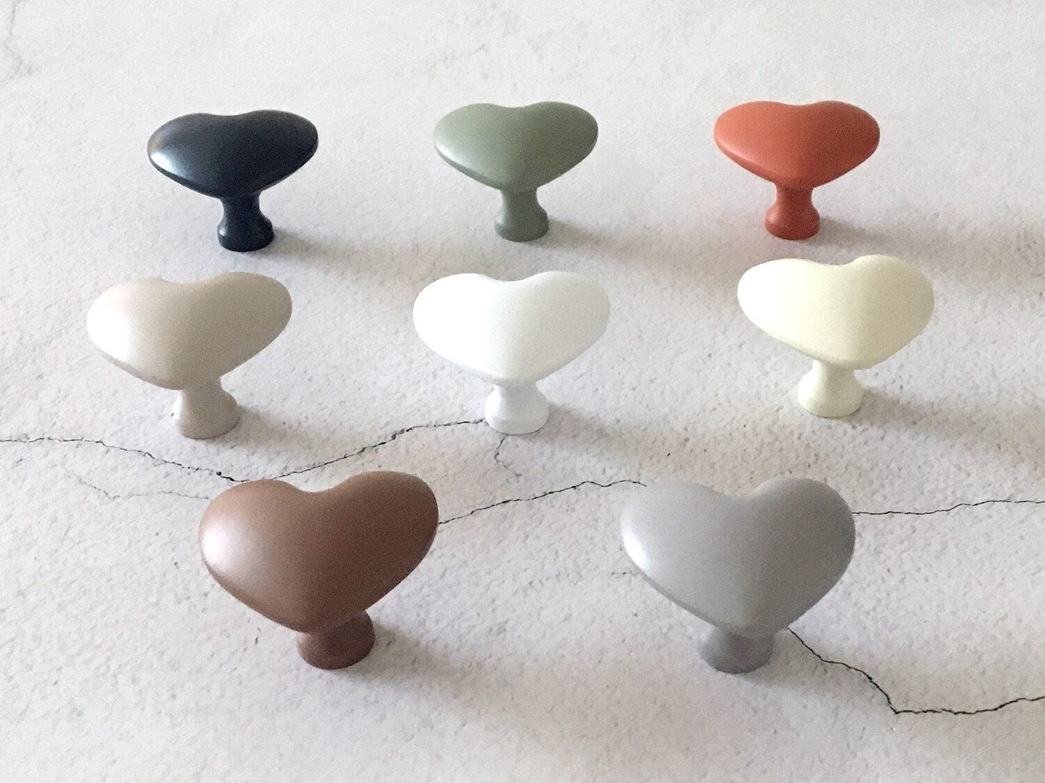 Set of heart-shaped cabinet knobs in various colors on a textured surface