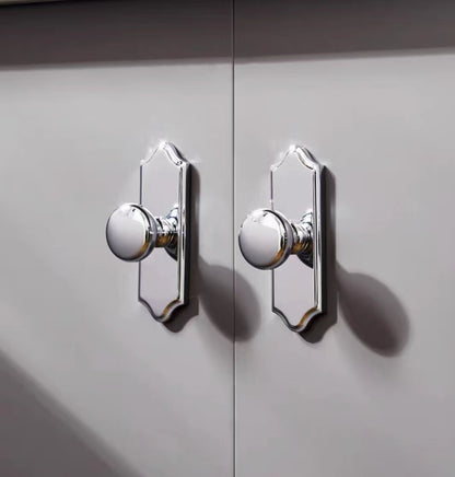 Close-up of two round shiny silver door knobs on a gray cabinet.