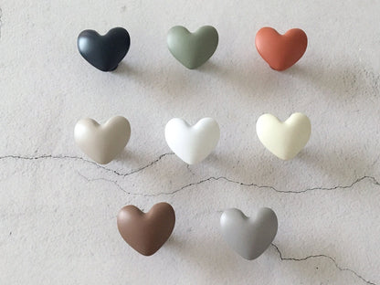 Set of heart-shaped cabinet knobs in various colors on a textured surface.