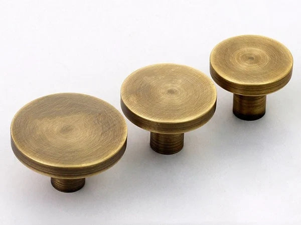 Three brass cabinet disc knobs on a white background
