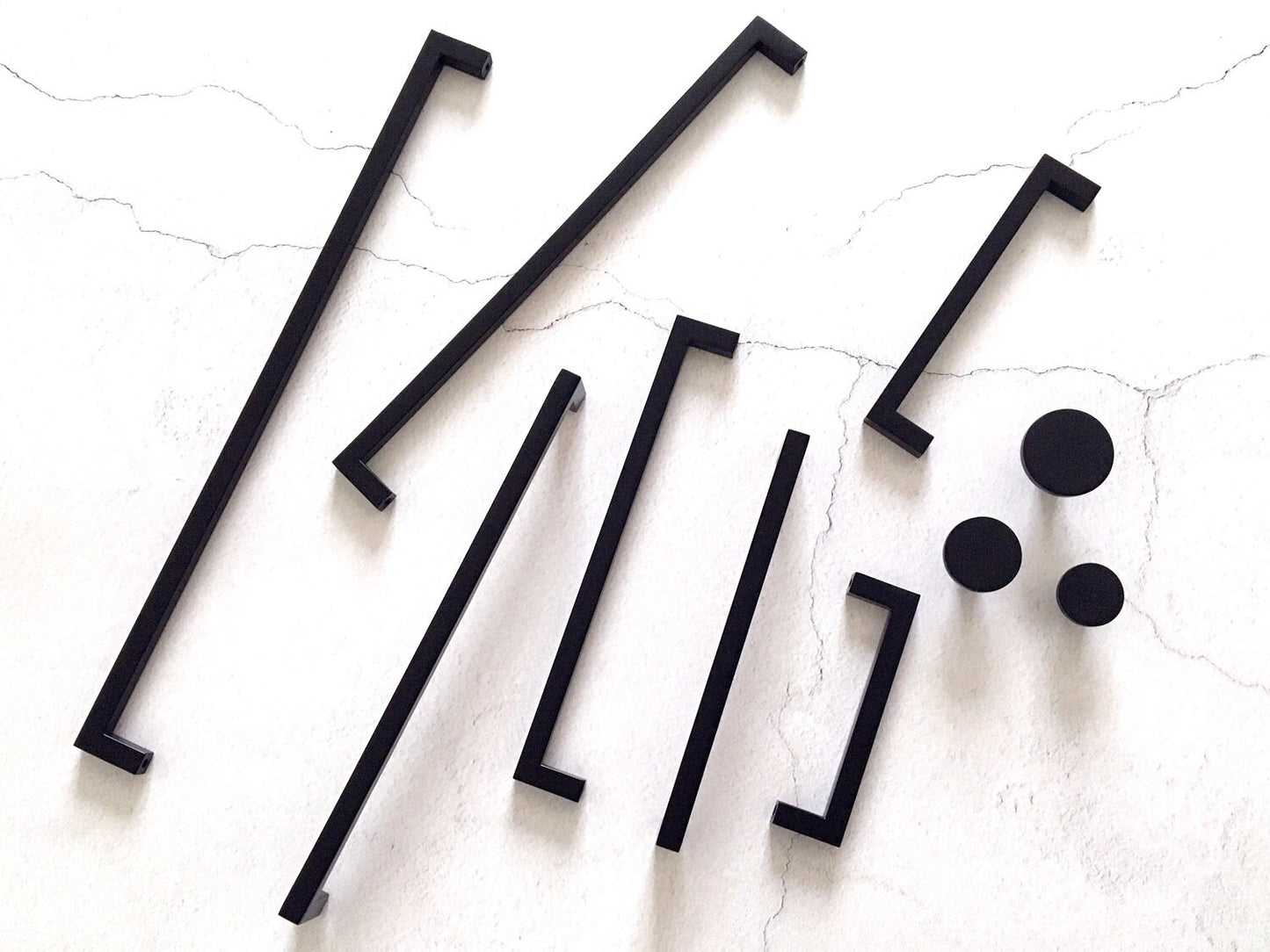 Set of black square bar handles and circular knobs on a textured white surface