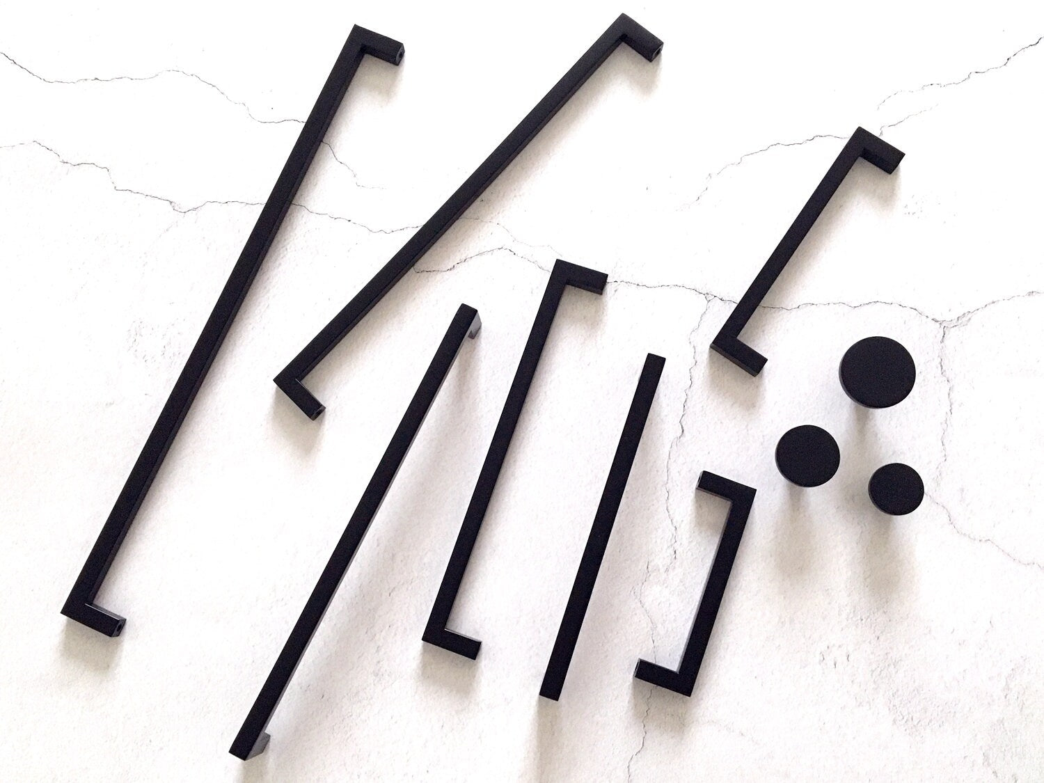 Set of black square bar handles and circular knobs on a textured white surface