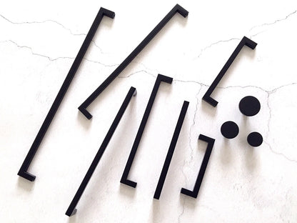 Set of black square bar handles and circular knobs on a textured white surface