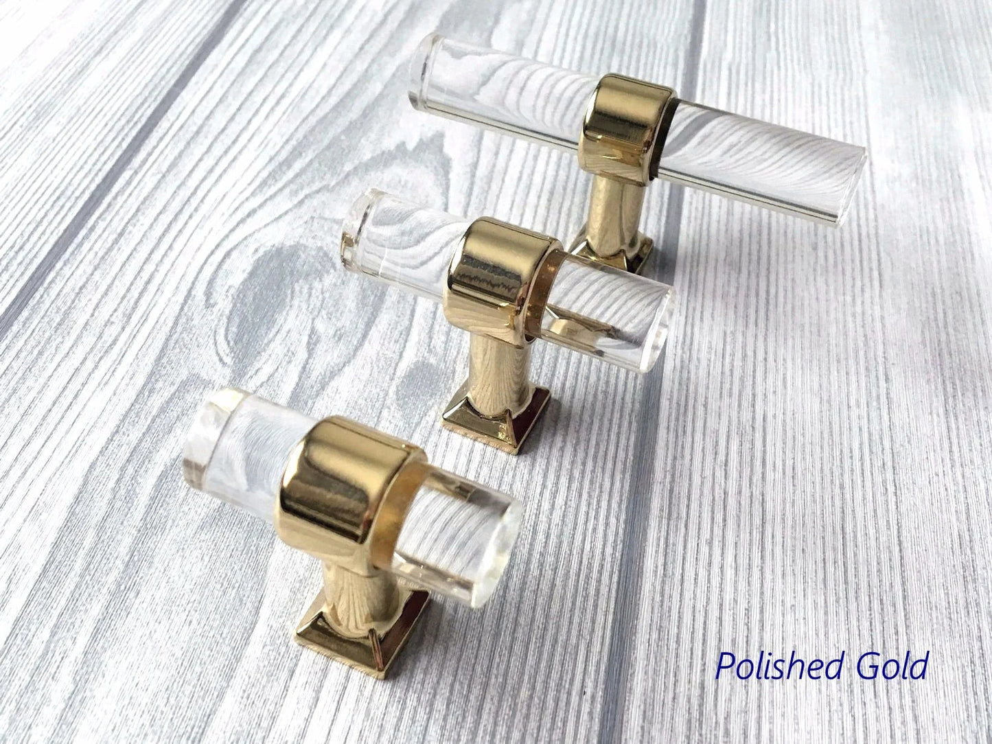 Polished gold and clear acrylic cabinet handles on a light wood surface