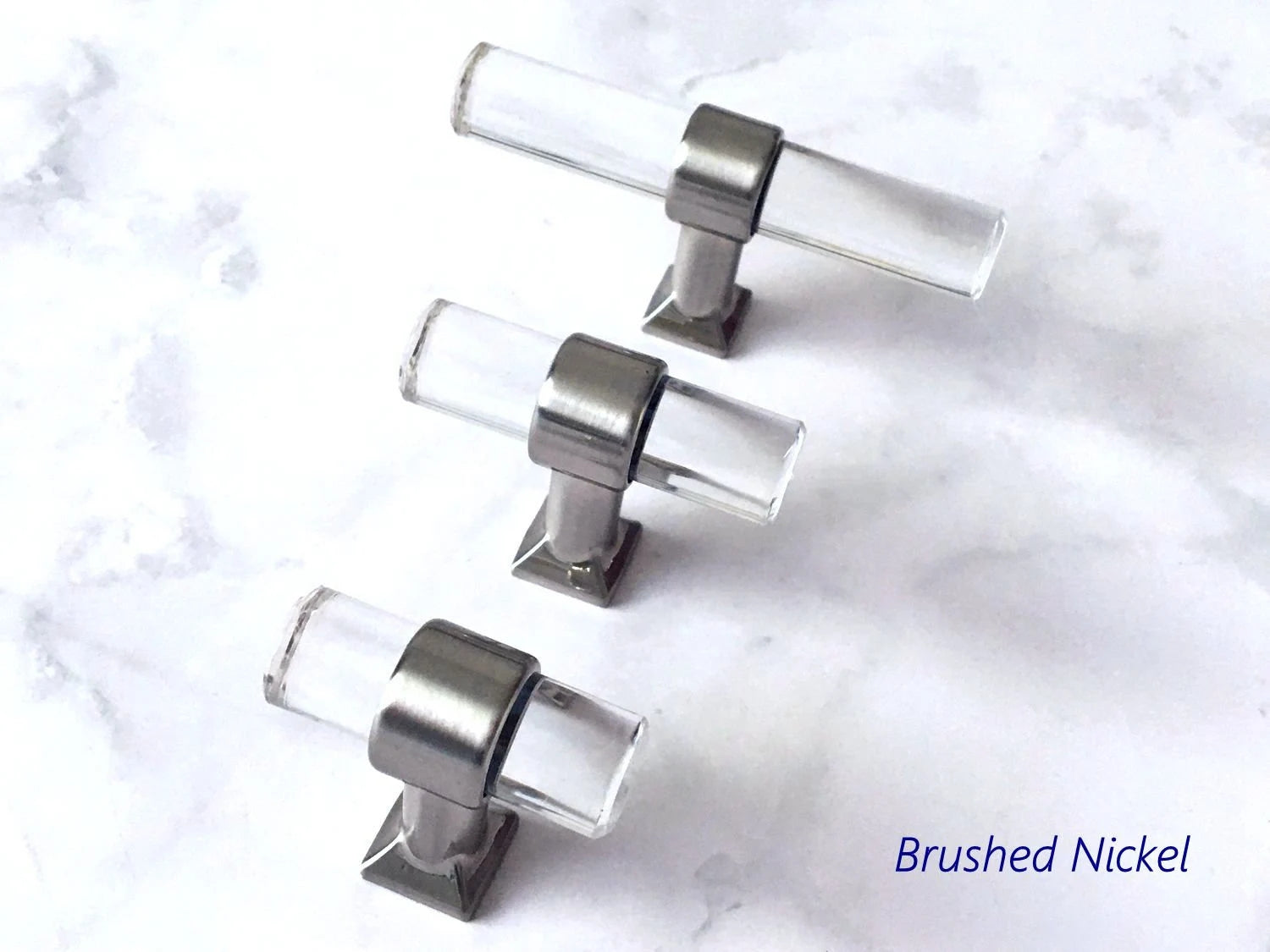 Set of four clear acrylic knobs with brushed nickel hardware on a marble surface.