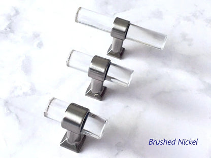 Set of four clear acrylic knobs with brushed nickel hardware on a marble surface.