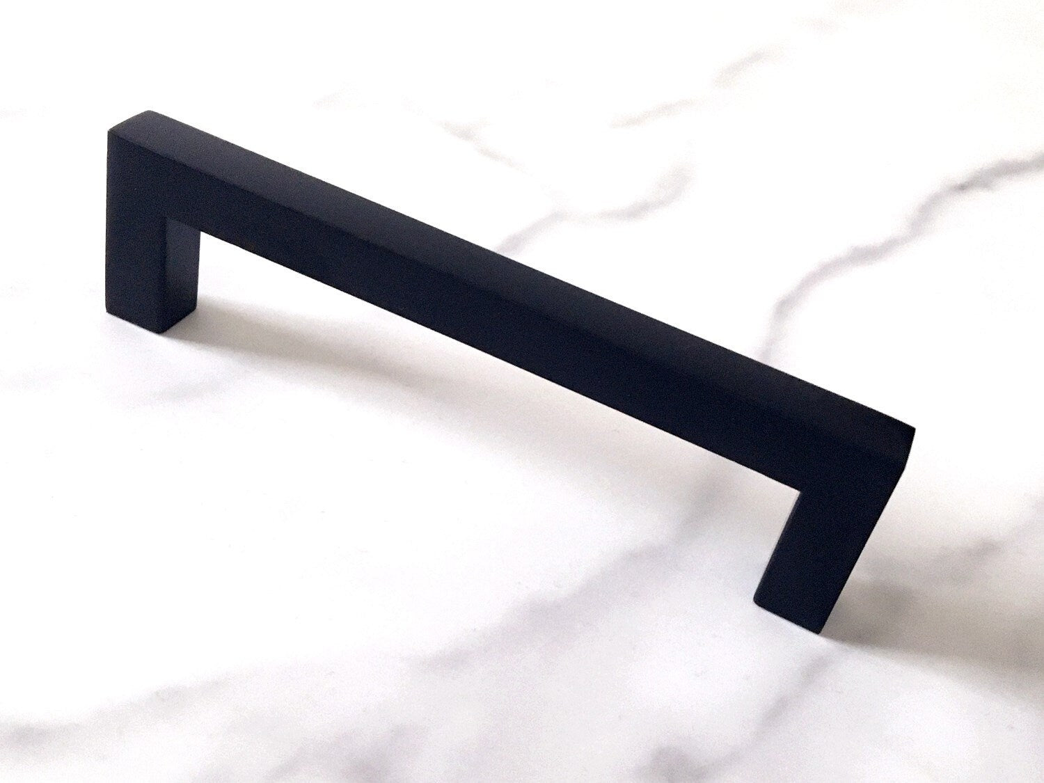 Black cabinet square handle on a white marble surface