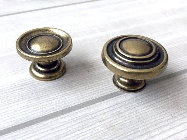 Two brass antique bronze cabinet knobs on a white wooden surface