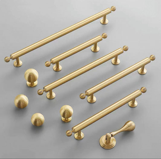 Set of brushed gold brass cabinet handles and round knobs on a gray background