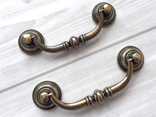 Pair of bronze cabinet swing handles on a white wooden surface