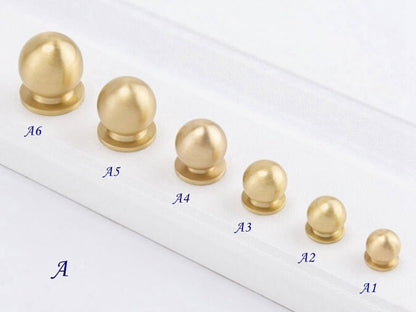 Set of gold ball knobs on a white surface with labeled sizes.

