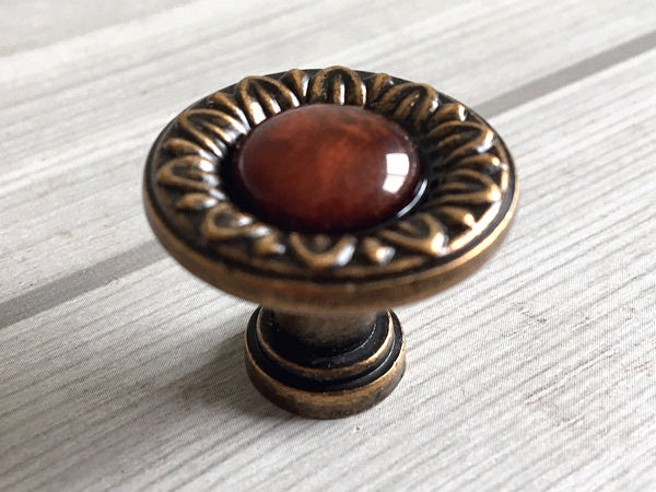 Decorative cabinet knob with red resin gemstone and bronze border on a light wooden surface