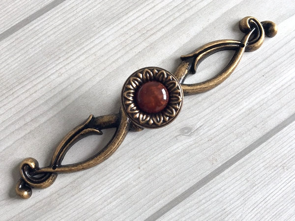 Decorative bronze pull handle with a red gemstone on a light wooden background