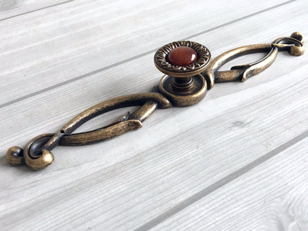Decorative brass handle with a red stone on a white wooden surface