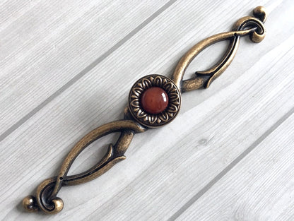 Decorative brass handle with a red resin gemstone on a light wooden surface