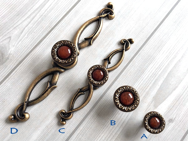 Decorative bronze pulls with red gemstones on a white wooden surface