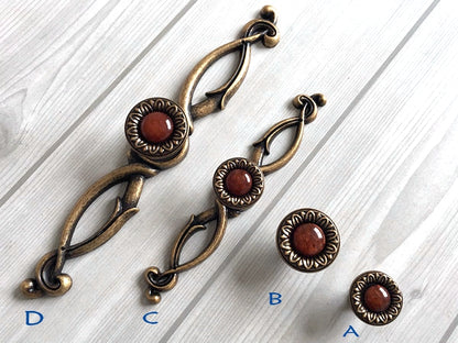 Decorative bronze pulls with red gemstones on a white wooden surface