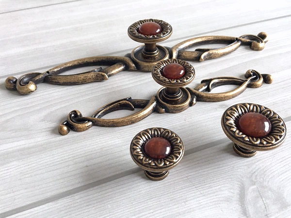 Set of vintage-style bronze cabinet knobs with red resin gem centers on a light wooden surface.