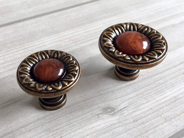 Two ornate cabinet knobs with red resin gemstones on a light wooden surface