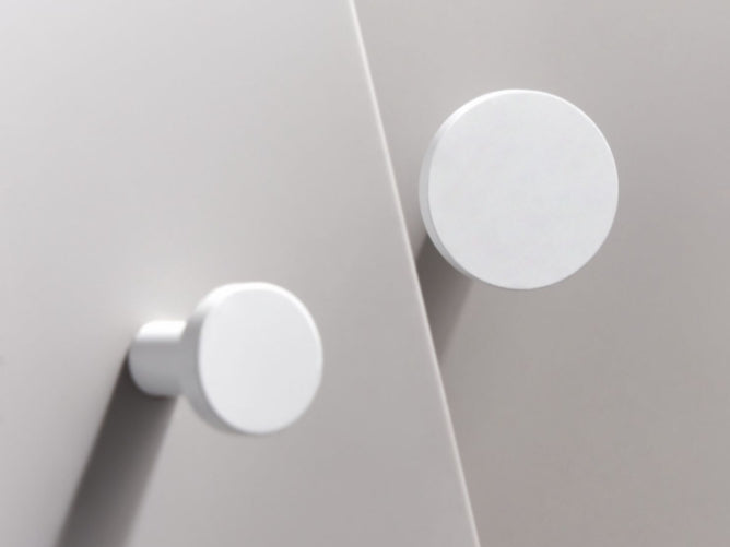Close-up of two white round knobs on a light gray surface.