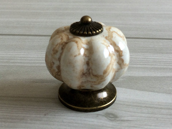 Decorative pumpkin-shaped knob with marble pattern and bronze base on a light wooden surface