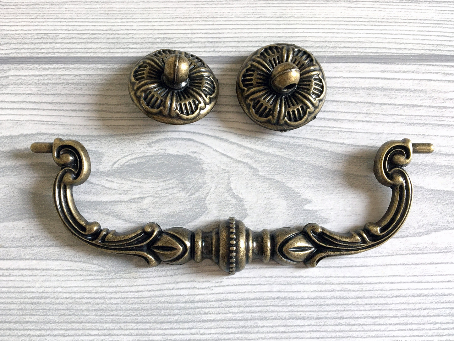 Decorative brass swing cabinet handle and two knobs on a light wood background