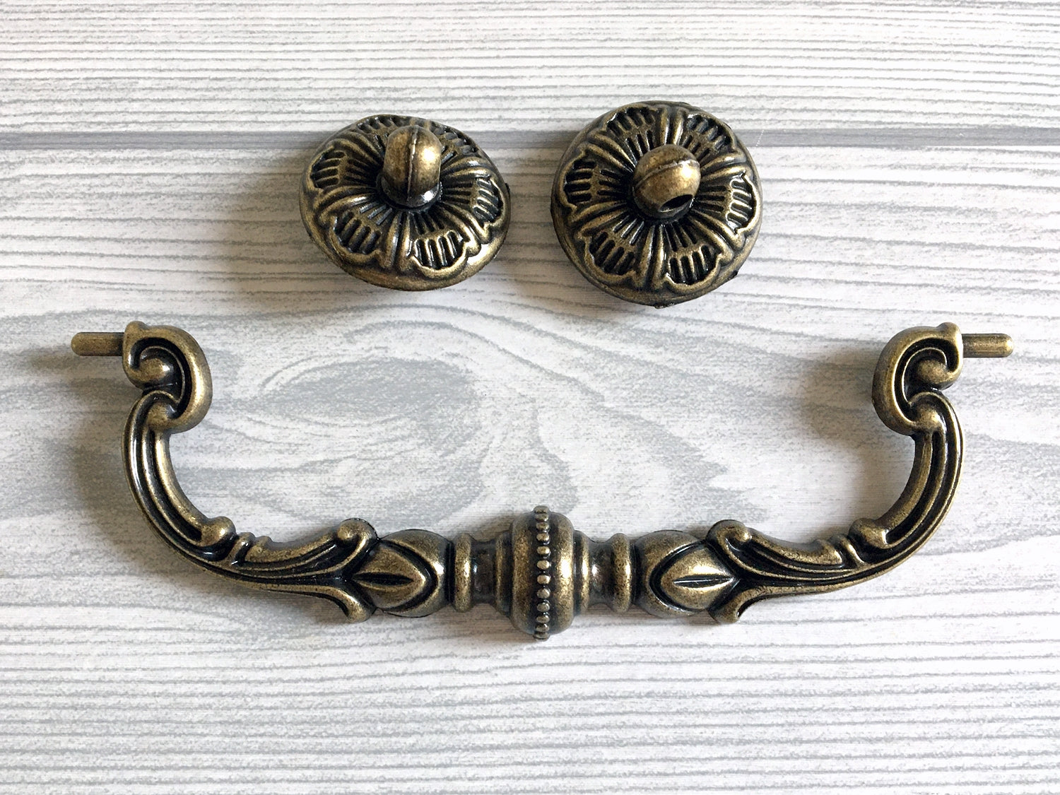 Decorative brass swing cabinet handle and two knobs on a light wood background
