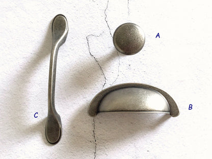 Metallic spoon, knob, and cup drawer pull  on a textured white surface.
