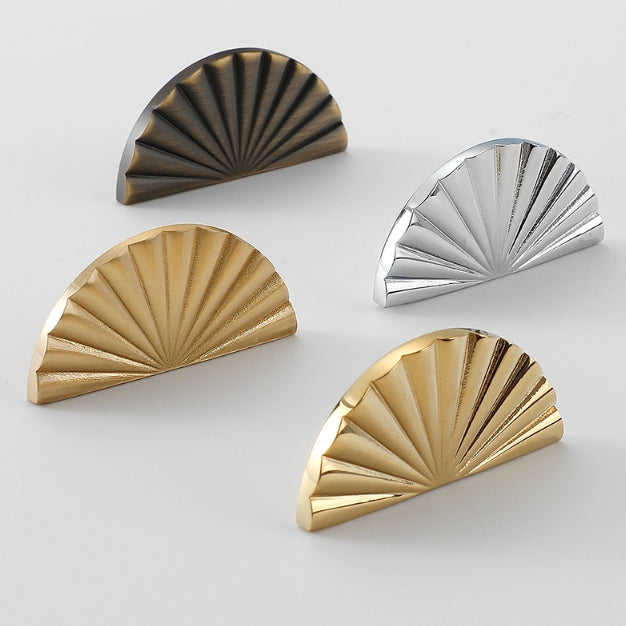 Four brass half-circle decorative cabinet knobs in gold, bronze, and silver on a light gray background.