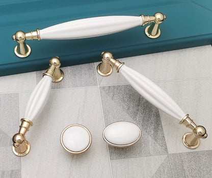 White ceramic cabinet handles with gold trim on a tiled floor.
