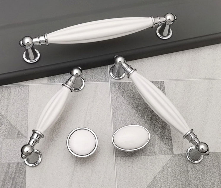 Set of white ceramic handles with silver metal accents on a tiled floor.