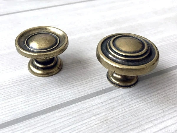 Two brass antique bronze cabinet knobs on a white wooden surface