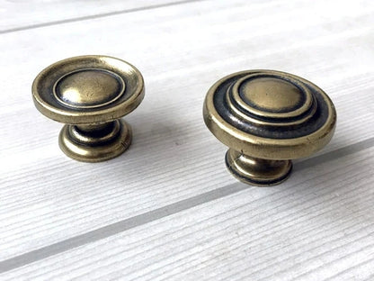 Two brass antique bronze cabinet knobs on a white wooden surface