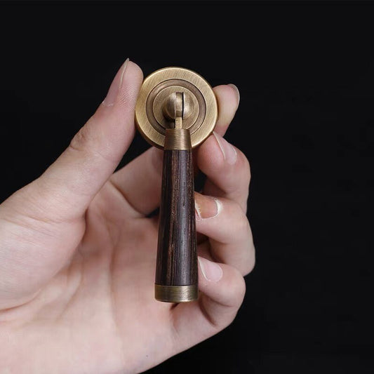 Hand holding a brass and wooden pendant pull against a black background
