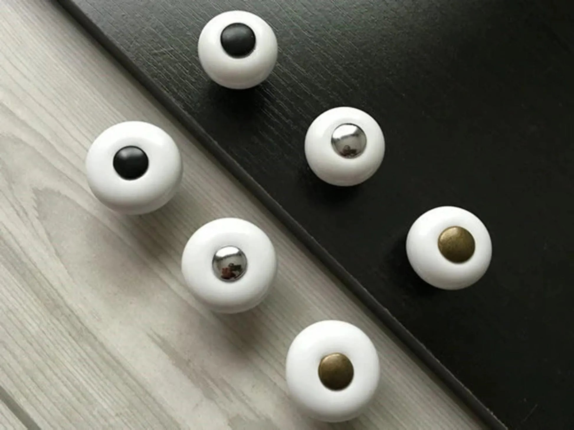 White porcelain knobs with black, silver, and gold centers on a wooden surface and black background