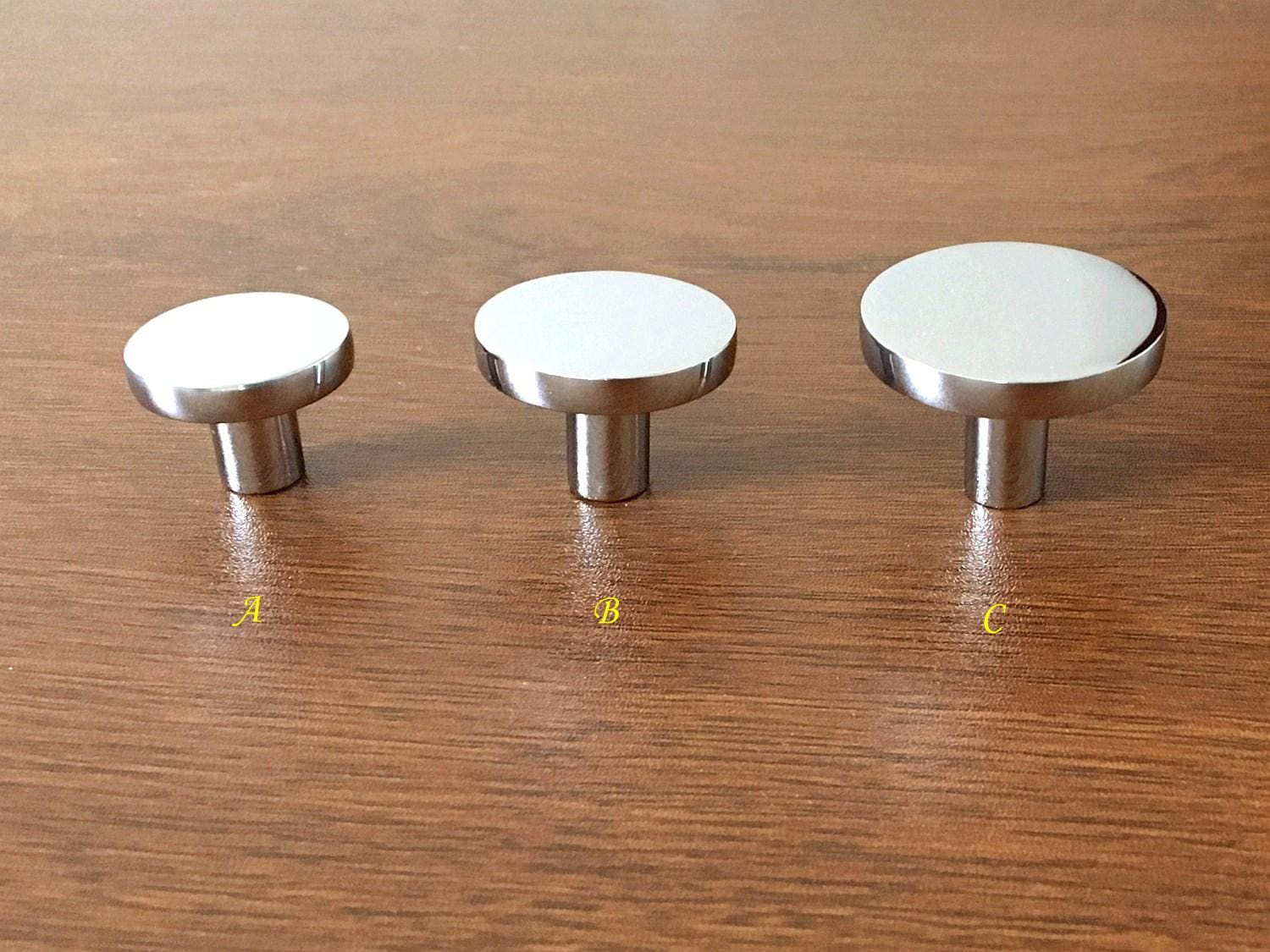 Three silver round cabinet disc knobs on a wooden surface