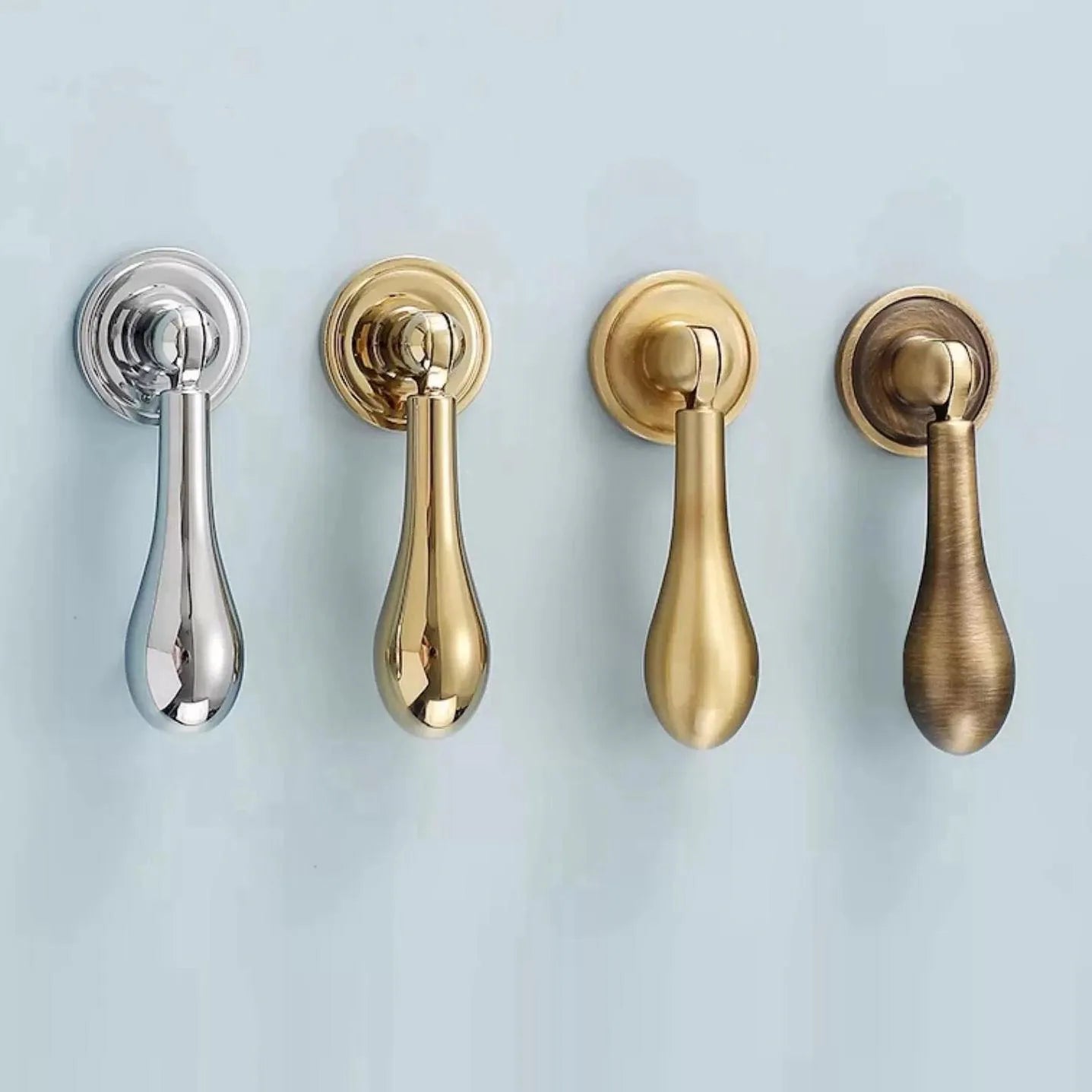 Four teardrop pulls in different finishes (silver, gold, brass) on a light blue background.