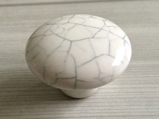 White ceramic knob with gray cracks on a textured surface
